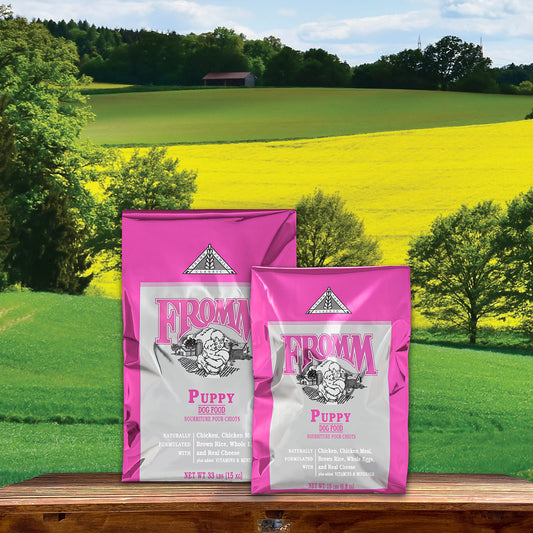 Two pink and silver Fromm Classic Puppy dry dog food bags on a wooden ledge overlooking green fields