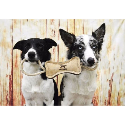 Two black-and-white dogs holding opposite rope loops of a Tall Tails leather and wool bone tug toy