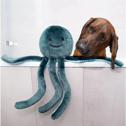 Brown dog beside a teal Fluff & Tuff Stevie Octopus plush toy draped over the edge of a bathtub.