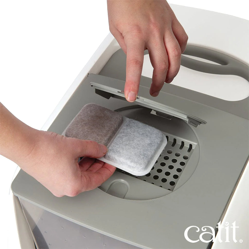 Hands inserting a two-section Catit Airsift odor-reducing filter pad beneath the top vent cover of a hooded litter box.
