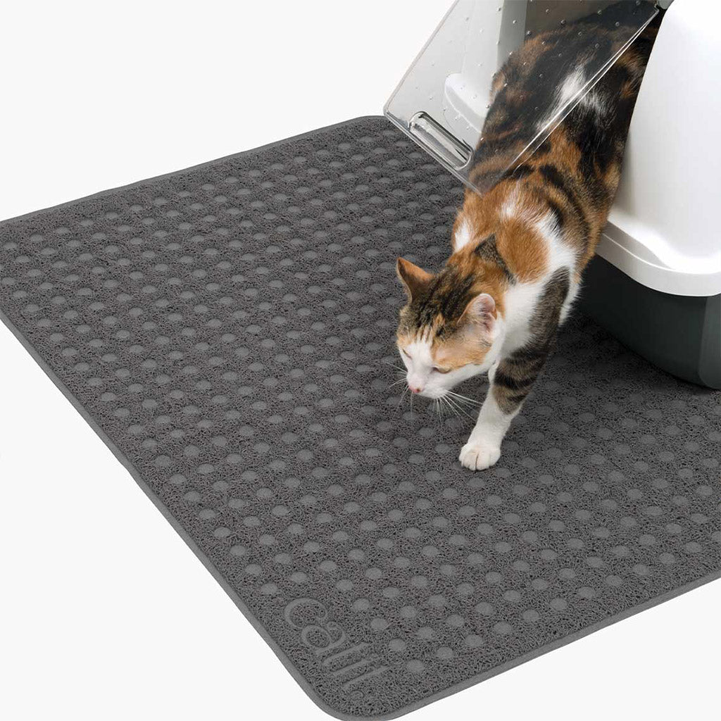 Calico cat stepping onto a large gray Catit litter mat in front of a covered litter box, showing its broad textured surface.