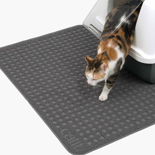 Calico cat stepping onto a large gray Catit litter mat in front of a covered litter box, showing its broad textured surface.
