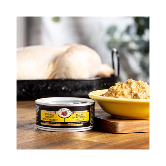 Fromm Shredded Chicken in Gravy Entrée cat food can beside a yellow bowl of shredded food on a wooden board