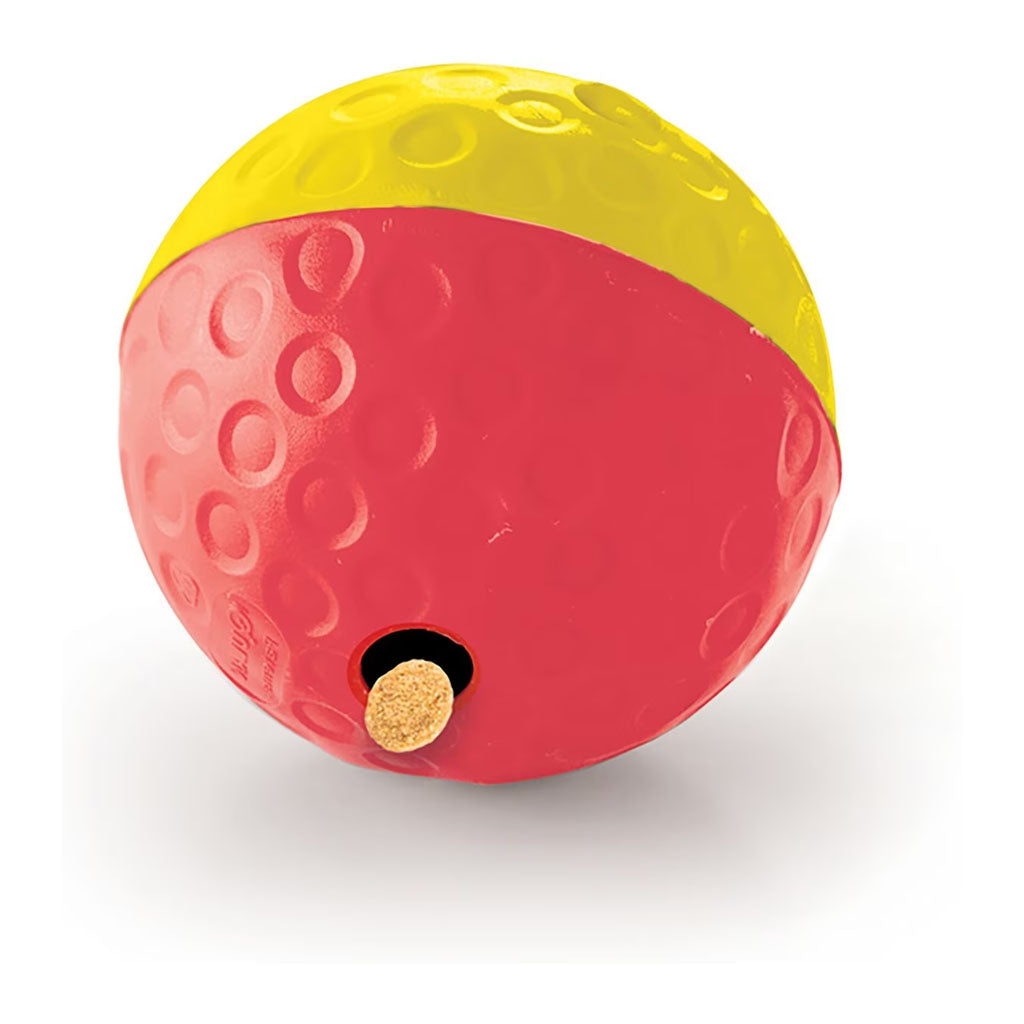 Large red and yellow Outward Hound Treat Tumble ball with textured circles and a treat emerging from the dispensing hole.