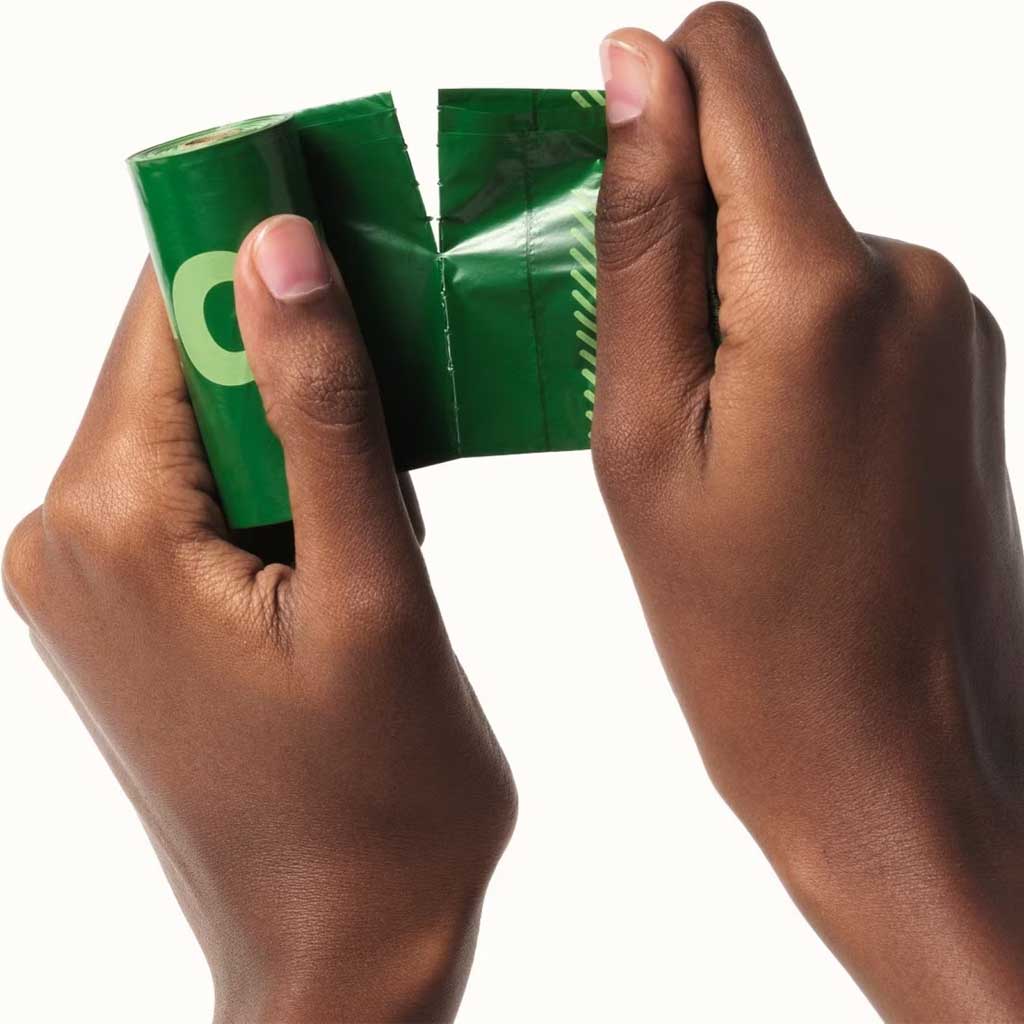 Hands separating a green Earth Rated dog poop bag from the roll along the perforation