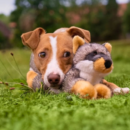 Brown and white dog lying on grass beside a Fluff & Tuff Sterling Fox plush dog toy.