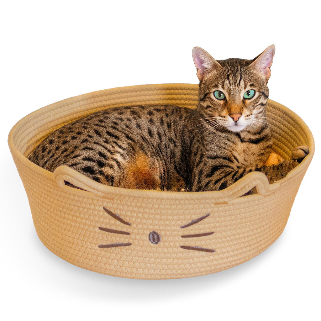 Tabby cat resting in a tan Catstages Bed & Basket Retreat rope basket bed with cat-ear handles and an embroidered cat face.